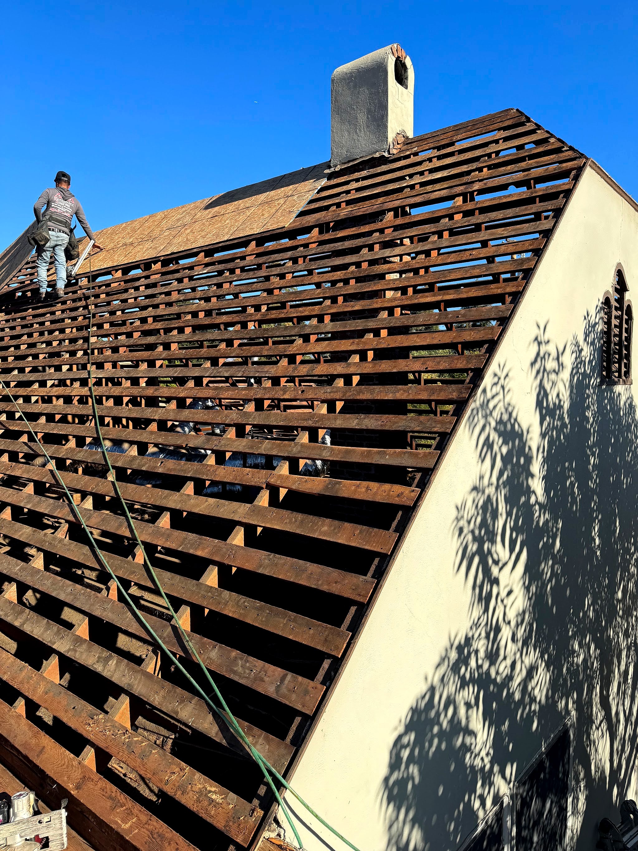 A roofer on a steep roof stripped down to the old board sheathing