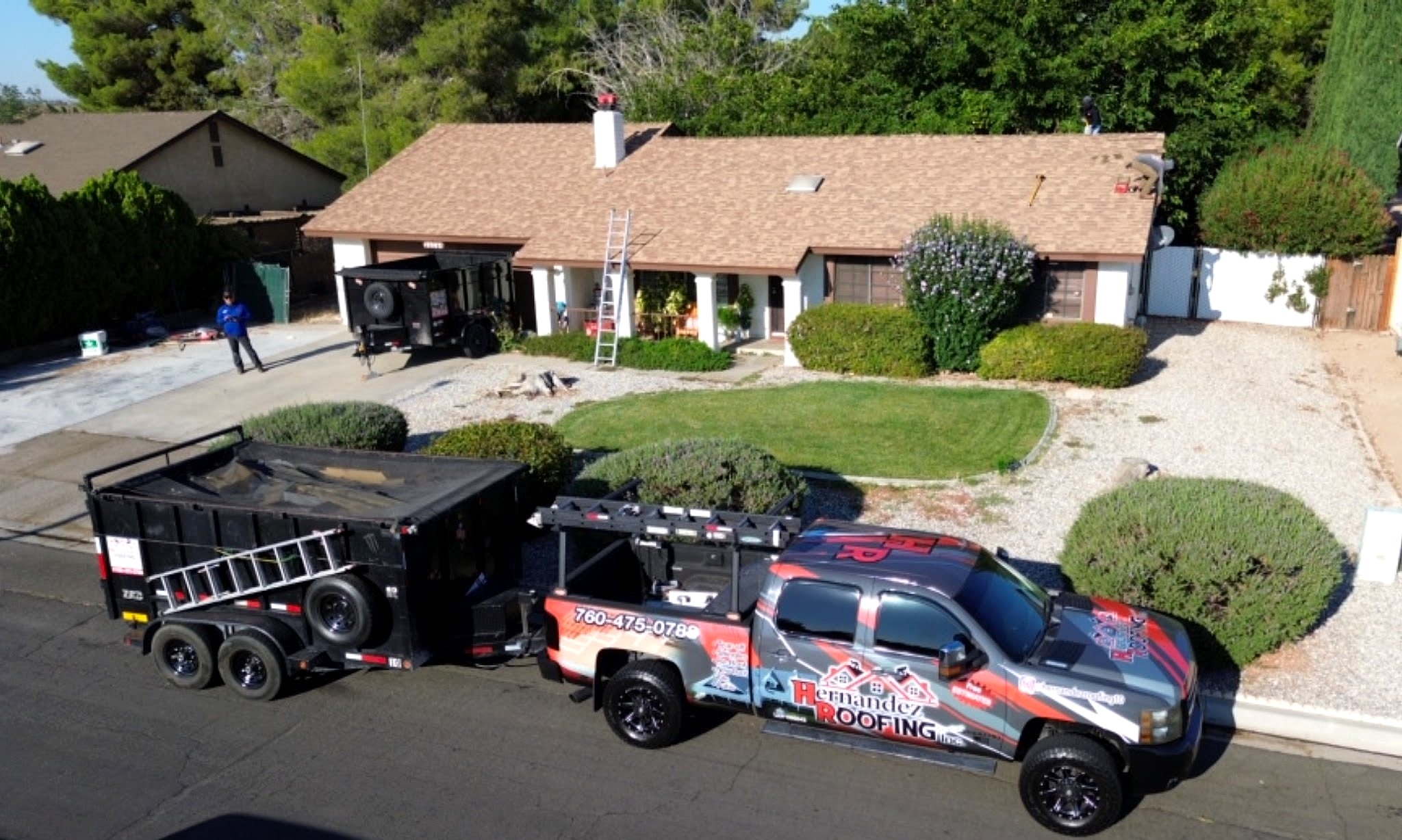 The wrapped Hernandez Roofing truck and dump trailer parked at a job, ladder up against the house
