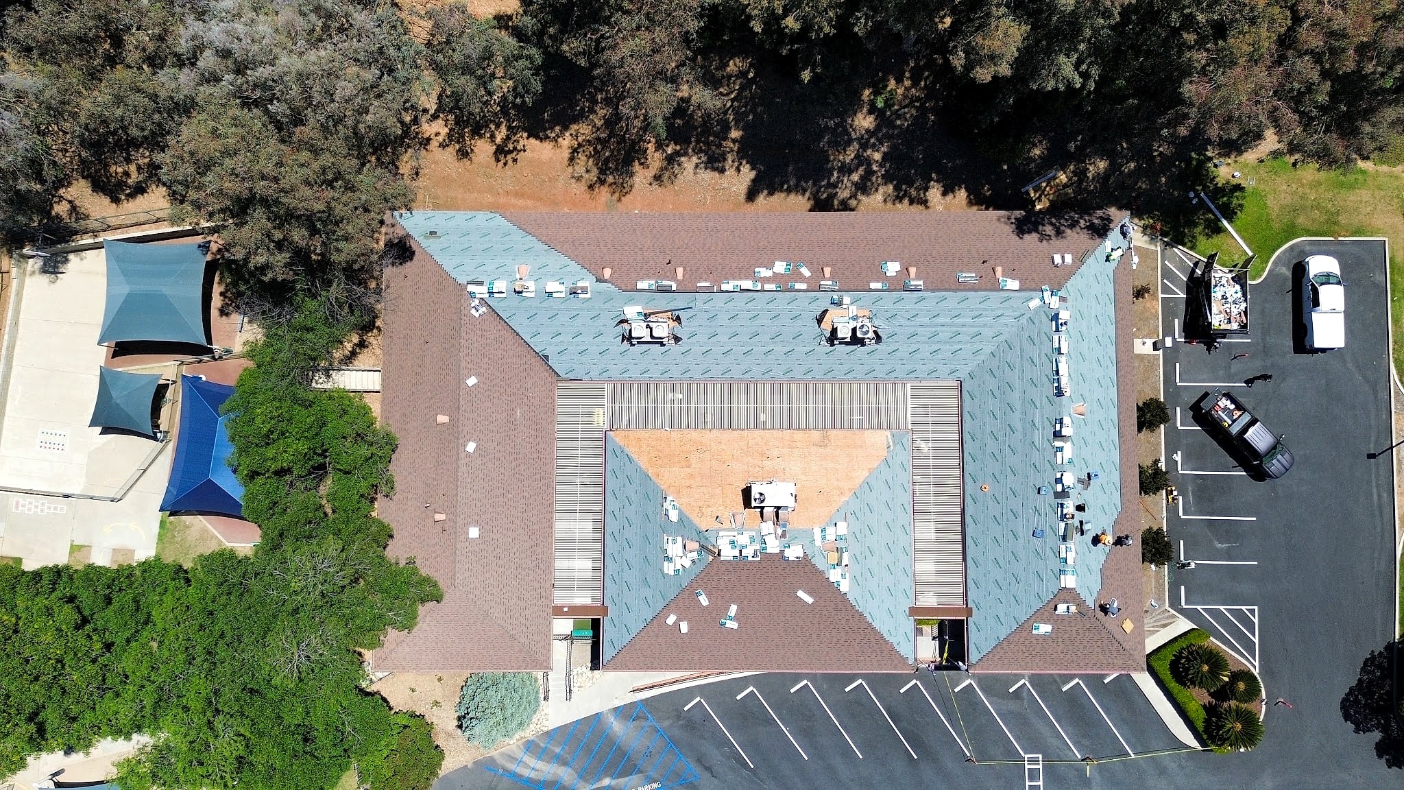Top-down drone view of a large U-shaped building mid re-roof, new shingles going on